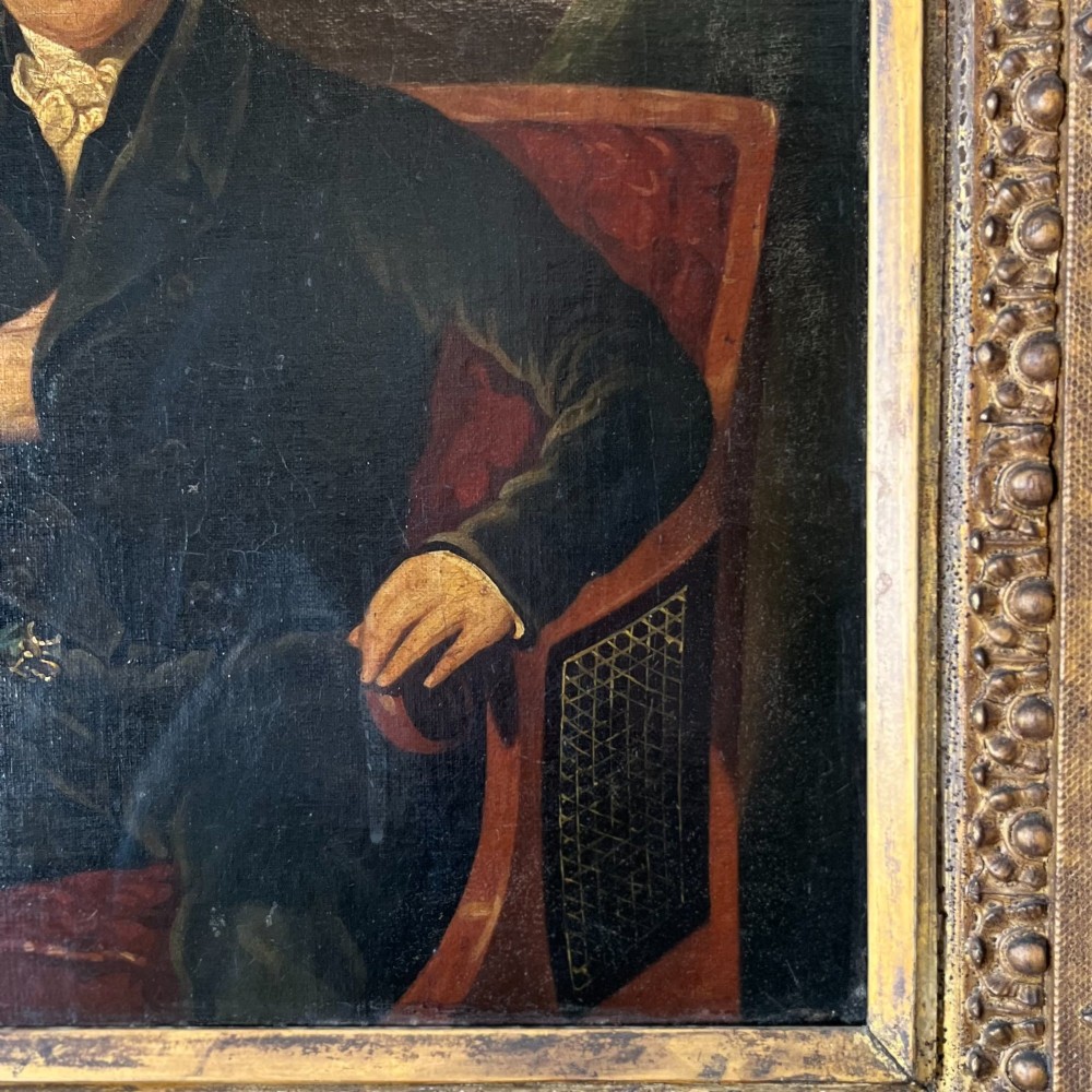 A 19th-century oil portrait depicting a seated gentleman in dark attire against a dark background, set within a heavily carved giltwood frame. View VI