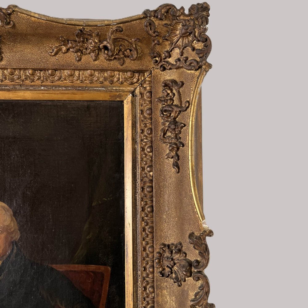 A 19th-century oil portrait depicting a seated gentleman in dark attire against a dark background, set within a heavily carved giltwood frame. View VIII