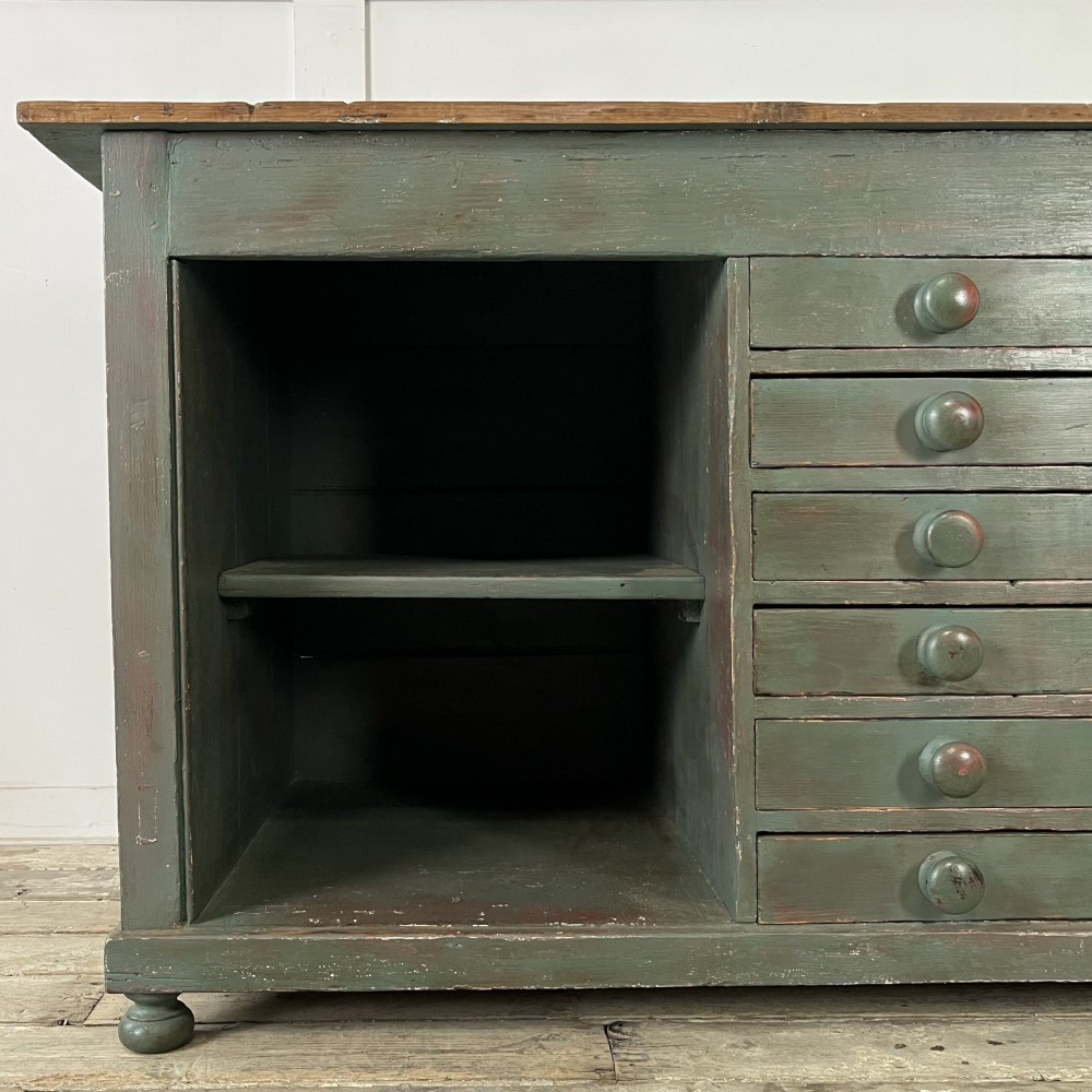A low Victorian dark green painted pine artist chest featuring six shallow drawers on the right, an open shelf compartment on the left, and an unpainted timber top. View IV