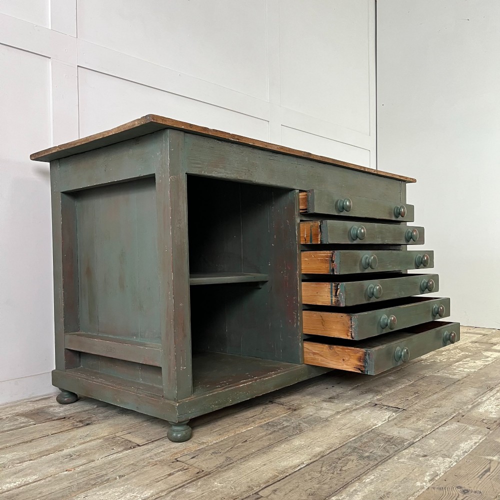 A low Victorian dark green painted pine artist chest featuring six shallow drawers on the right, an open shelf compartment on the left, and an unpainted timber top. View V