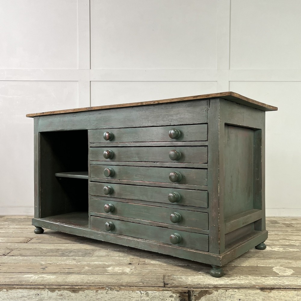 A low Victorian dark green painted pine artist chest featuring six shallow drawers on the right, an open shelf compartment on the left, and an unpainted timber top. View XI