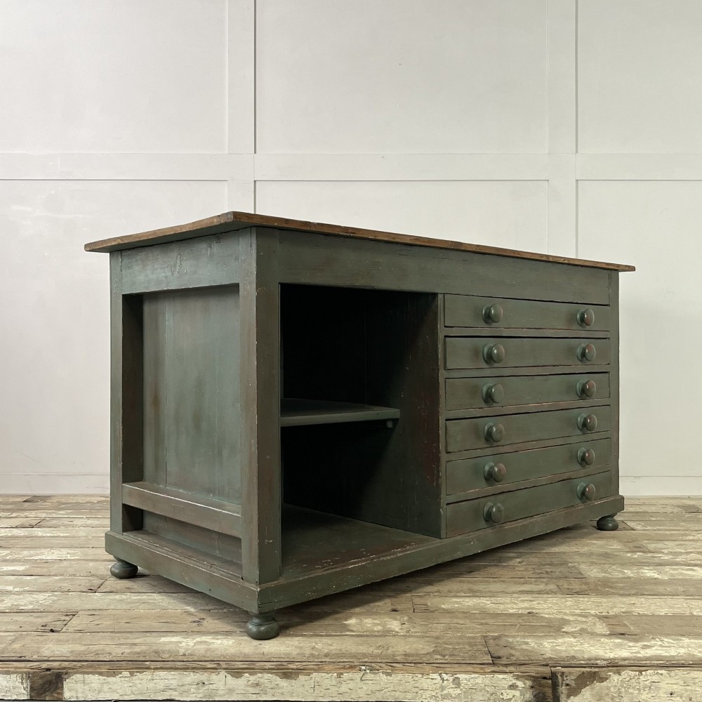 A low Victorian dark green painted pine artist chest featuring six shallow drawers on the right, an open shelf compartment on the left, and an unpainted timber top. View XV