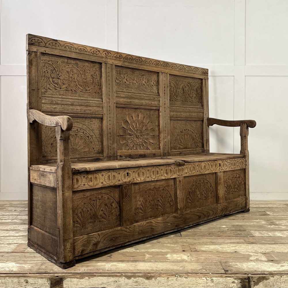 An early nineteenth-century carved oak high-back settle featuring carved back panels, curved arms, and an integrated box storage seat.