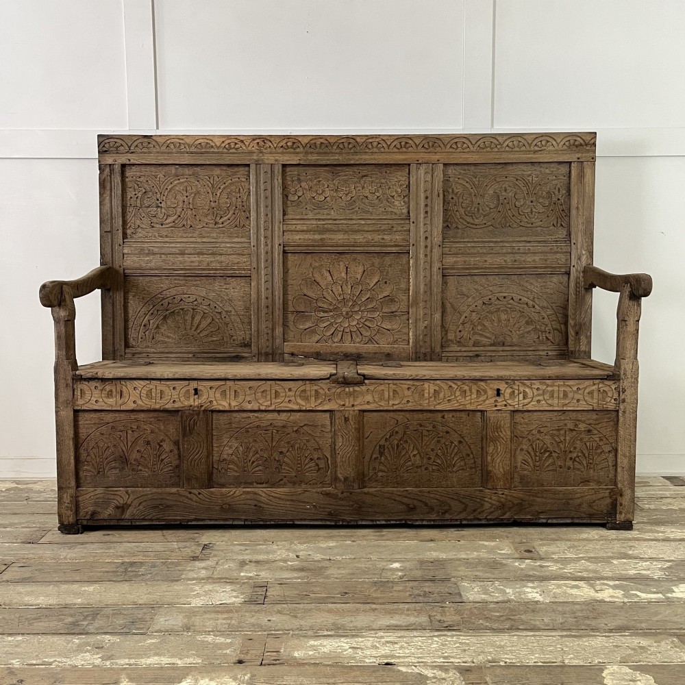 An early nineteenth-century carved oak high-back settle featuring carved back panels, curved arms, and an integrated box storage seat. View II
