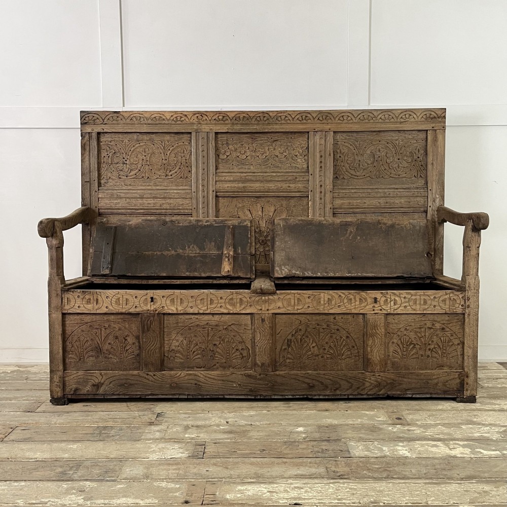 An early nineteenth-century carved oak high-back settle featuring carved back panels, curved arms, and an integrated box storage seat. View III