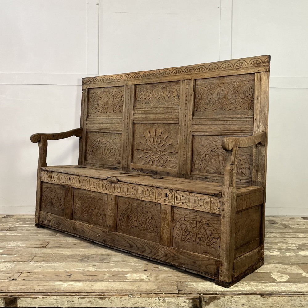 An early nineteenth-century carved oak high-back settle featuring carved back panels, curved arms, and an integrated box storage seat. View IV