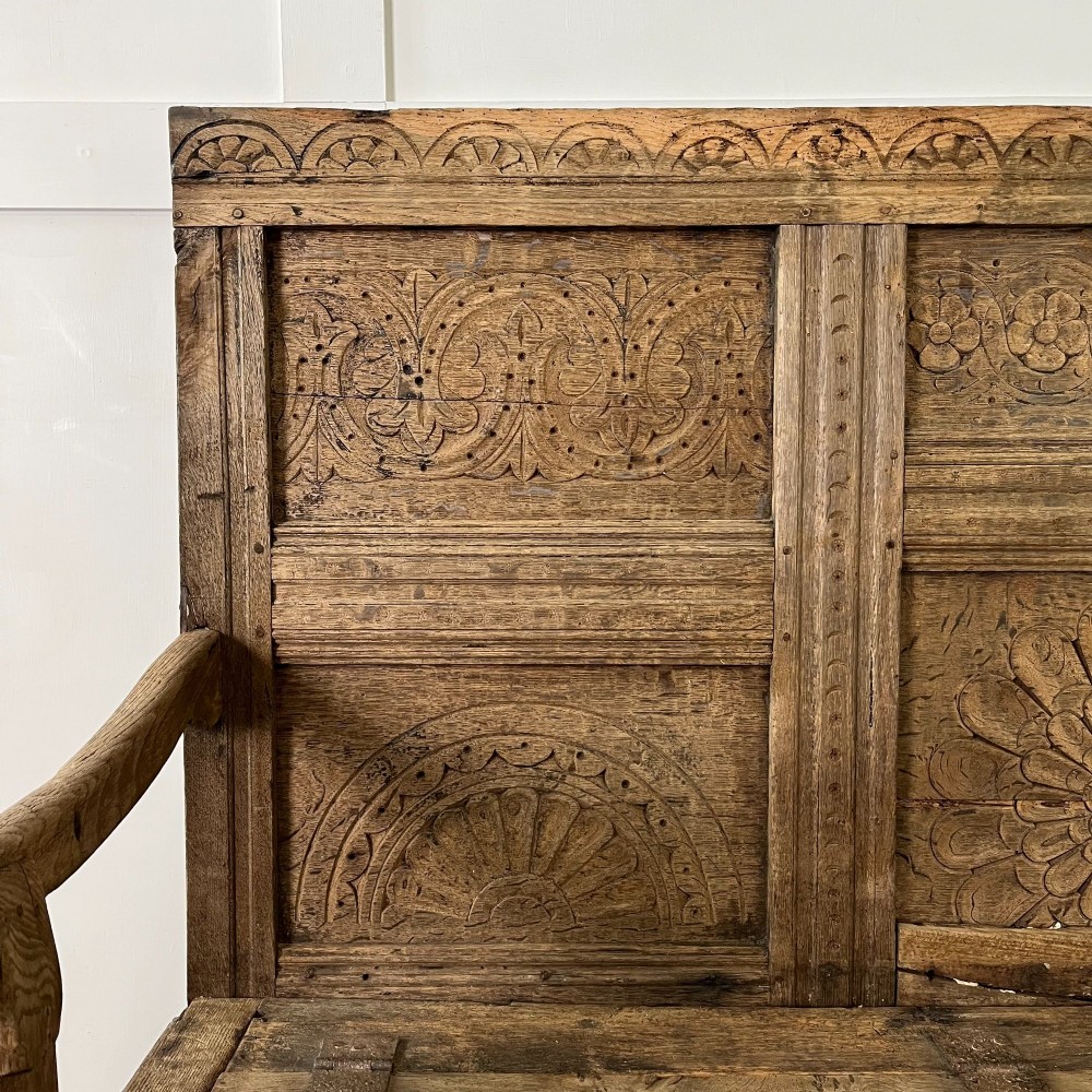 An early nineteenth-century carved oak high-back settle featuring carved back panels, curved arms, and an integrated box storage seat. View V