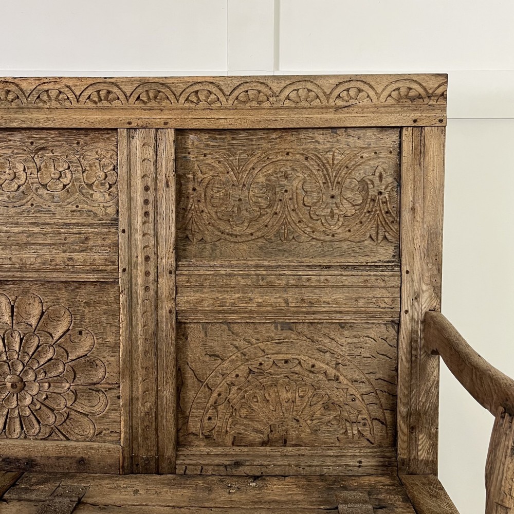 An early nineteenth-century carved oak high-back settle featuring carved back panels, curved arms, and an integrated box storage seat. View VII