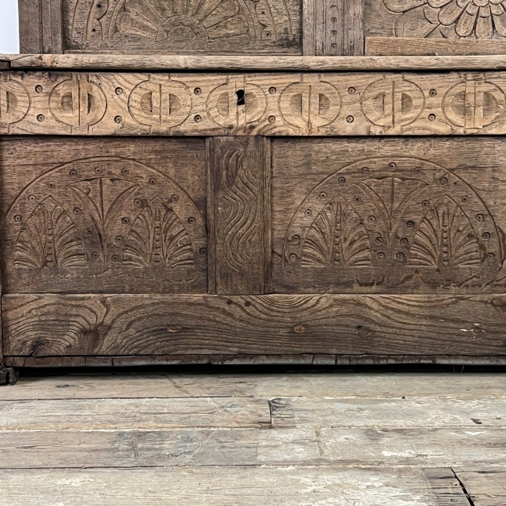 An early nineteenth-century carved oak high-back settle featuring carved back panels, curved arms, and an integrated box storage seat. View IX