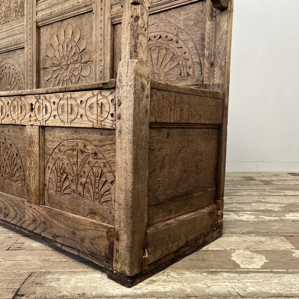 An early nineteenth-century carved oak high-back settle featuring carved back panels, curved arms, and an integrated box storage seat. View X