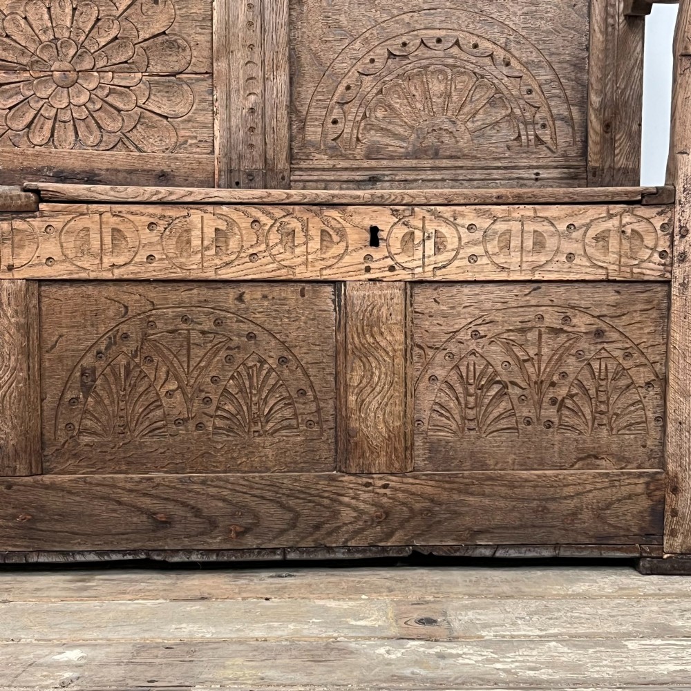 An early nineteenth-century carved oak high-back settle featuring carved back panels, curved arms, and an integrated box storage seat. View XI