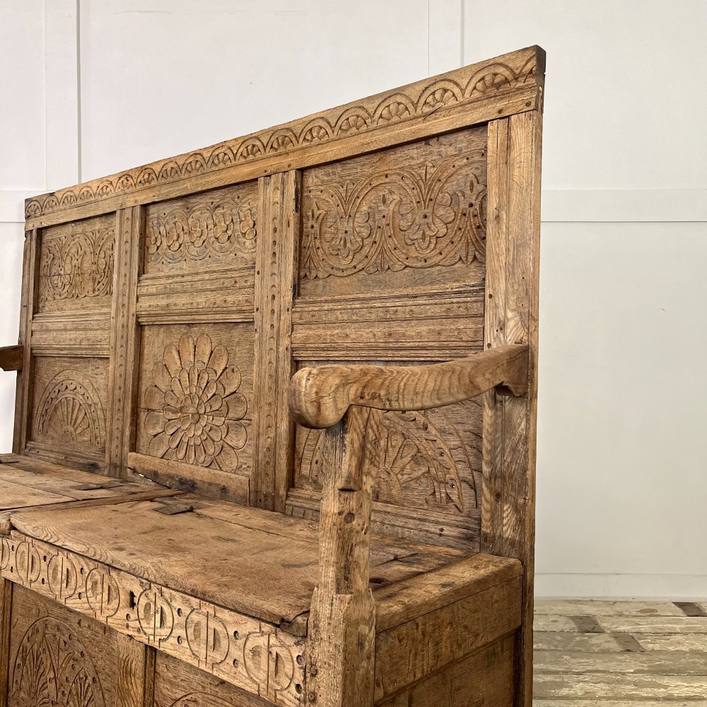 An early nineteenth-century carved oak high-back settle featuring carved back panels, curved arms, and an integrated box storage seat. View XII