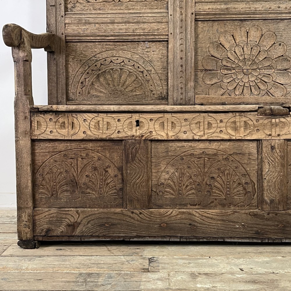An early nineteenth-century carved oak high-back settle featuring carved back panels, curved arms, and an integrated box storage seat. View XIII