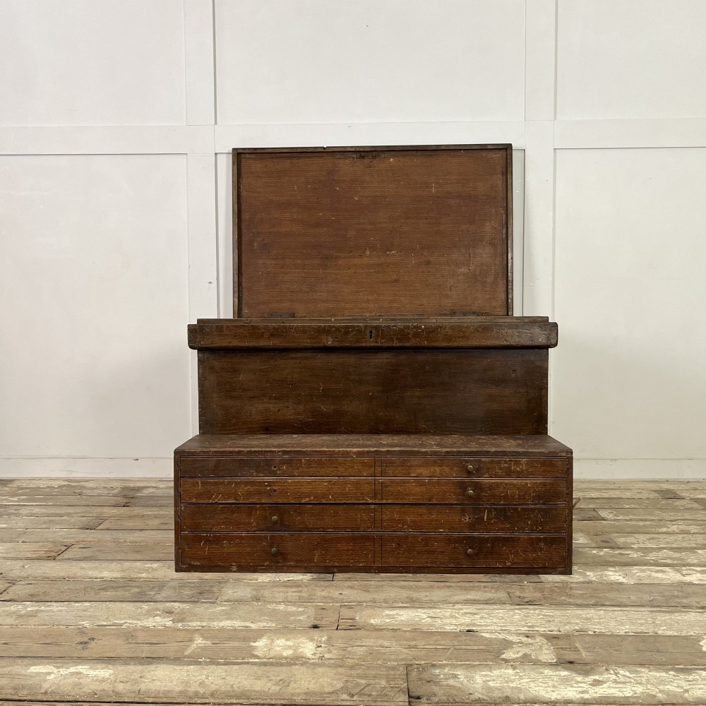 An early 20th-century pine carpenters chest featuring an upper hinged lid and multiple shallow lower drawers with small round knobs.