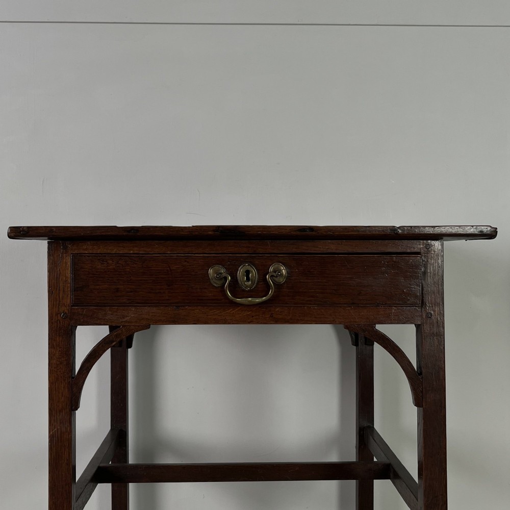 An early 19th century dark oak side table featuring a single drawer with a brass handle, arched aprons, and straight square legs connected by a low stretcher. View II