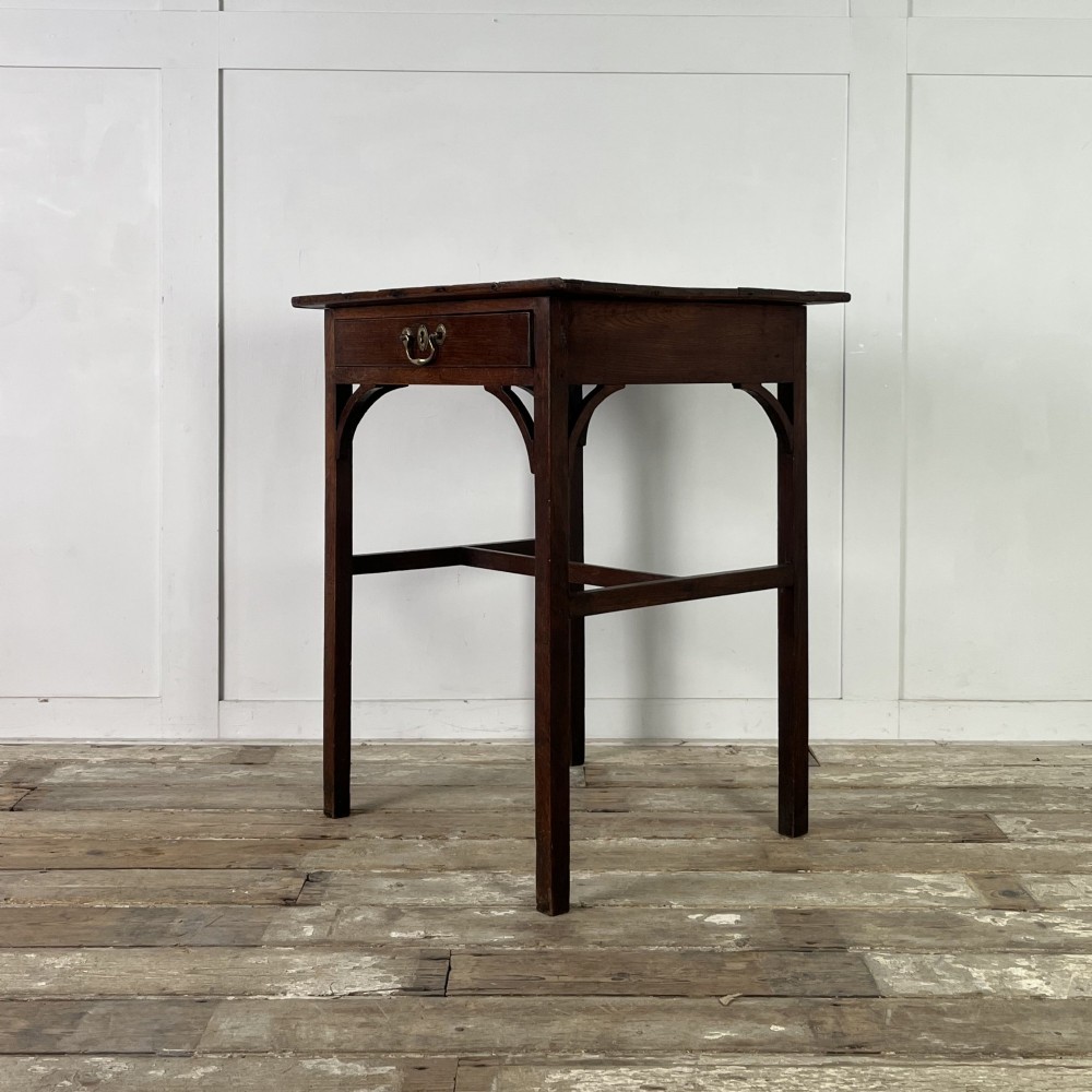 An early 19th century dark oak side table featuring a single drawer with a brass handle, arched aprons, and straight square legs connected by a low stretcher. View V