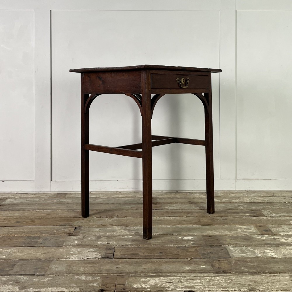 An early 19th century dark oak side table featuring a single drawer with a brass handle, arched aprons, and straight square legs connected by a low stretcher. View VI