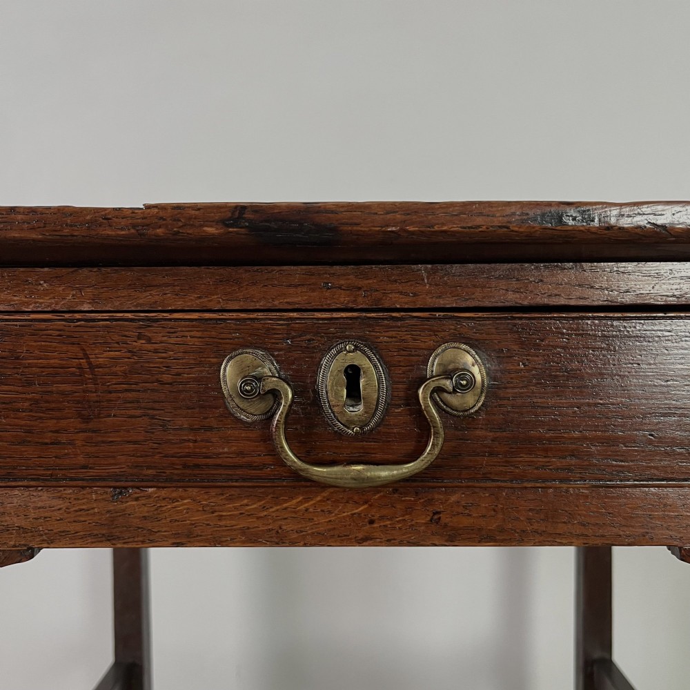 An early 19th century dark oak side table featuring a single drawer with a brass handle, arched aprons, and straight square legs connected by a low stretcher. View IX