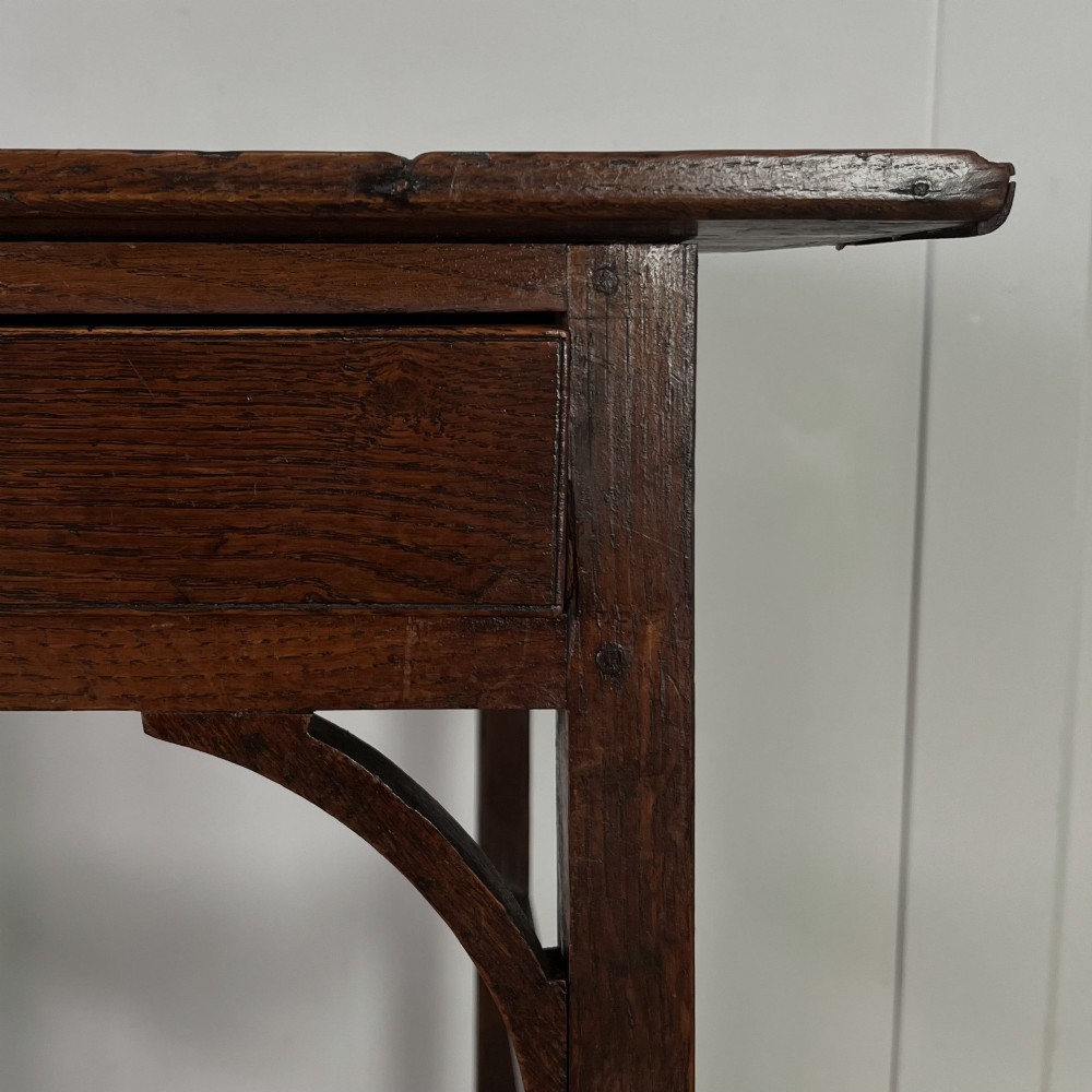An early 19th century dark oak side table featuring a single drawer with a brass handle, arched aprons, and straight square legs connected by a low stretcher. View X