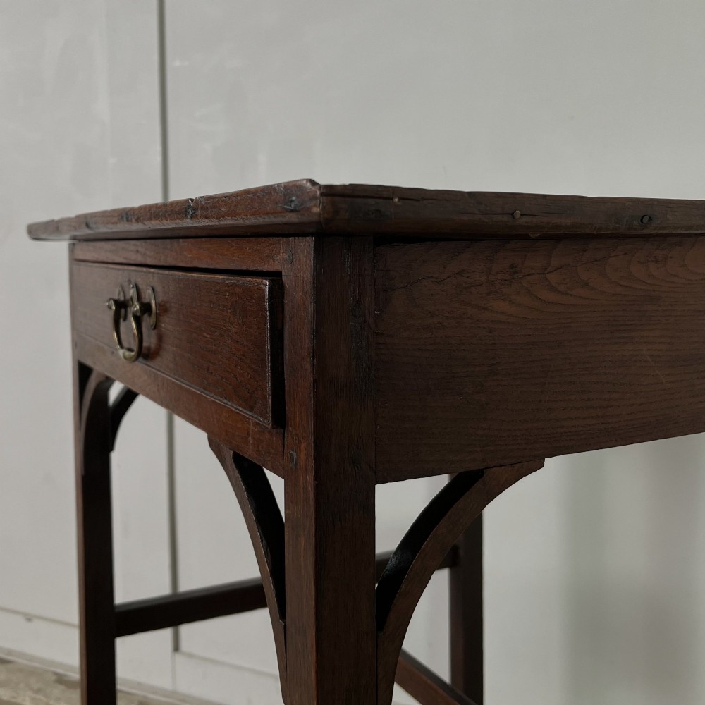 An early 19th century dark oak side table featuring a single drawer with a brass handle, arched aprons, and straight square legs connected by a low stretcher. View XIII
