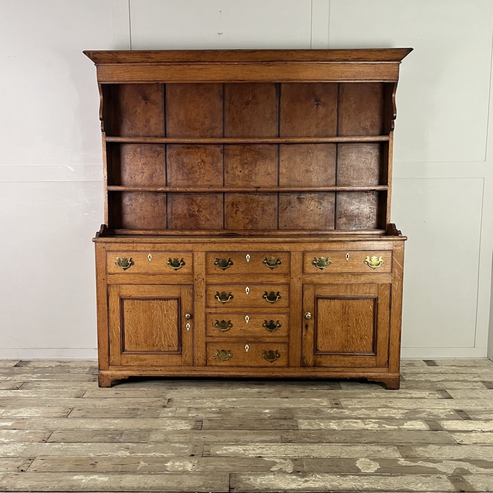An early nineteenth-century oak kitchen dresser featuring an open upper plate rack over a base with central drawers and side cupboard doors with brass hardware.
