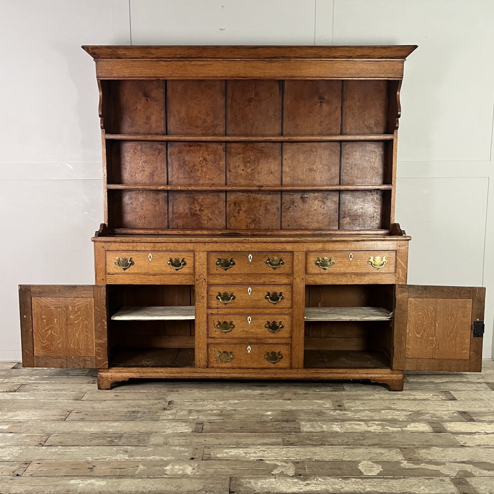 An early nineteenth-century oak kitchen dresser featuring an open upper plate rack over a base with central drawers and side cupboard doors with brass hardware. View II
