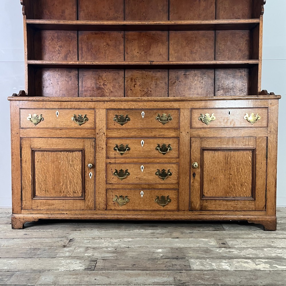 An early nineteenth-century oak kitchen dresser featuring an open upper plate rack over a base with central drawers and side cupboard doors with brass hardware. View IV