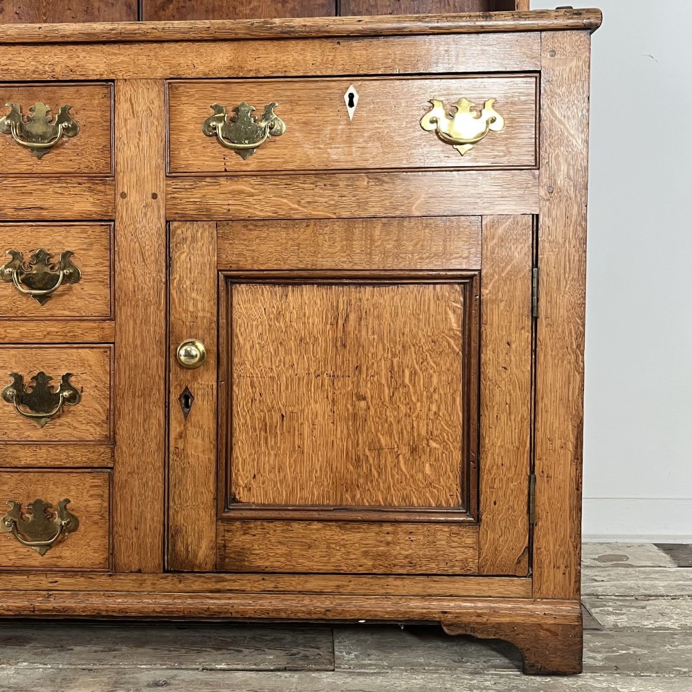 An early nineteenth-century oak kitchen dresser featuring an open upper plate rack over a base with central drawers and side cupboard doors with brass hardware. View VII