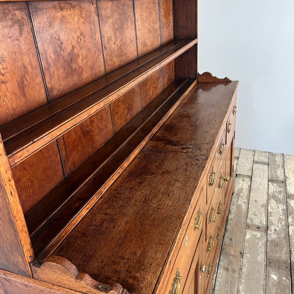 An early nineteenth-century oak kitchen dresser featuring an open upper plate rack over a base with central drawers and side cupboard doors with brass hardware. View VIII
