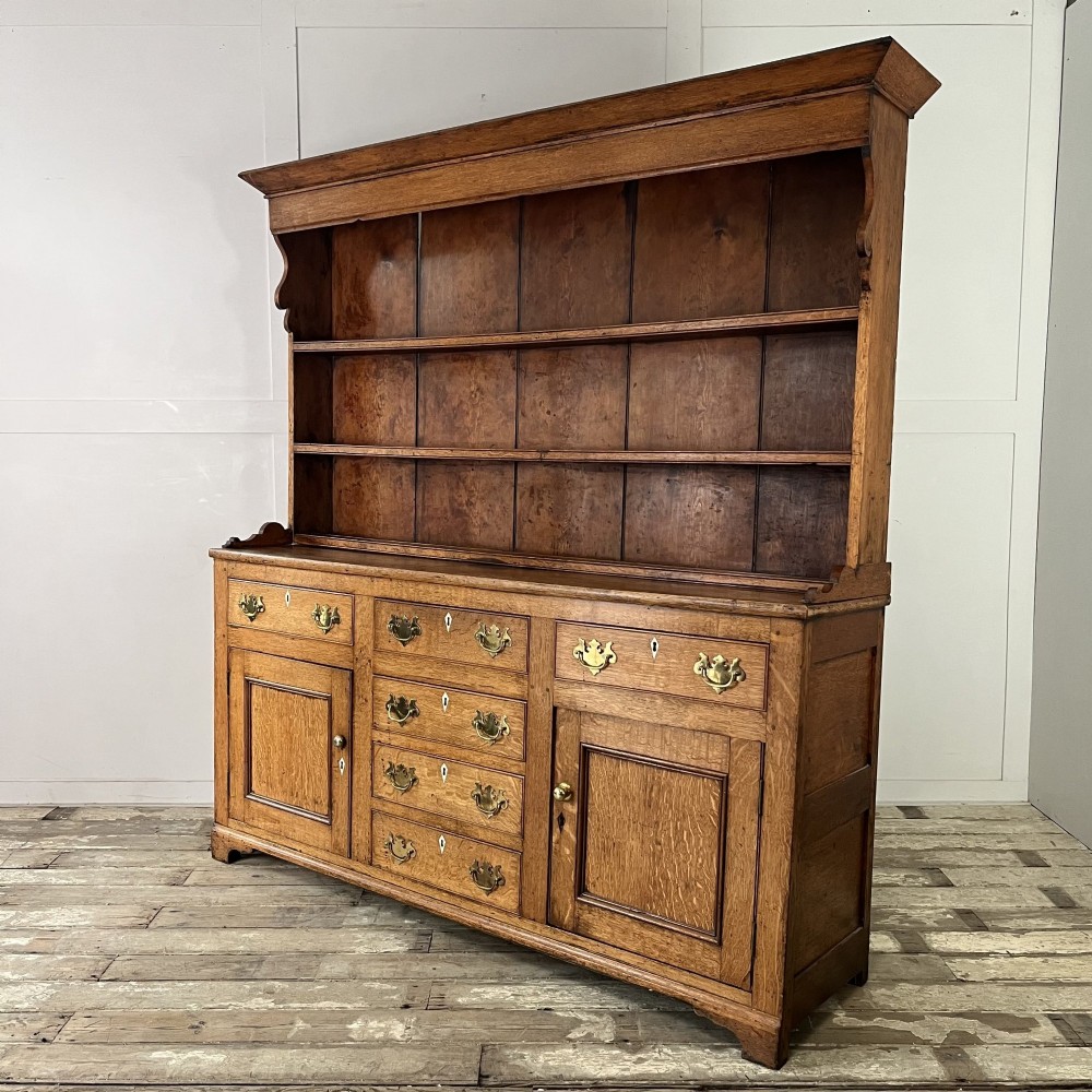 An early nineteenth-century oak kitchen dresser featuring an open upper plate rack over a base with central drawers and side cupboard doors with brass hardware. View X
