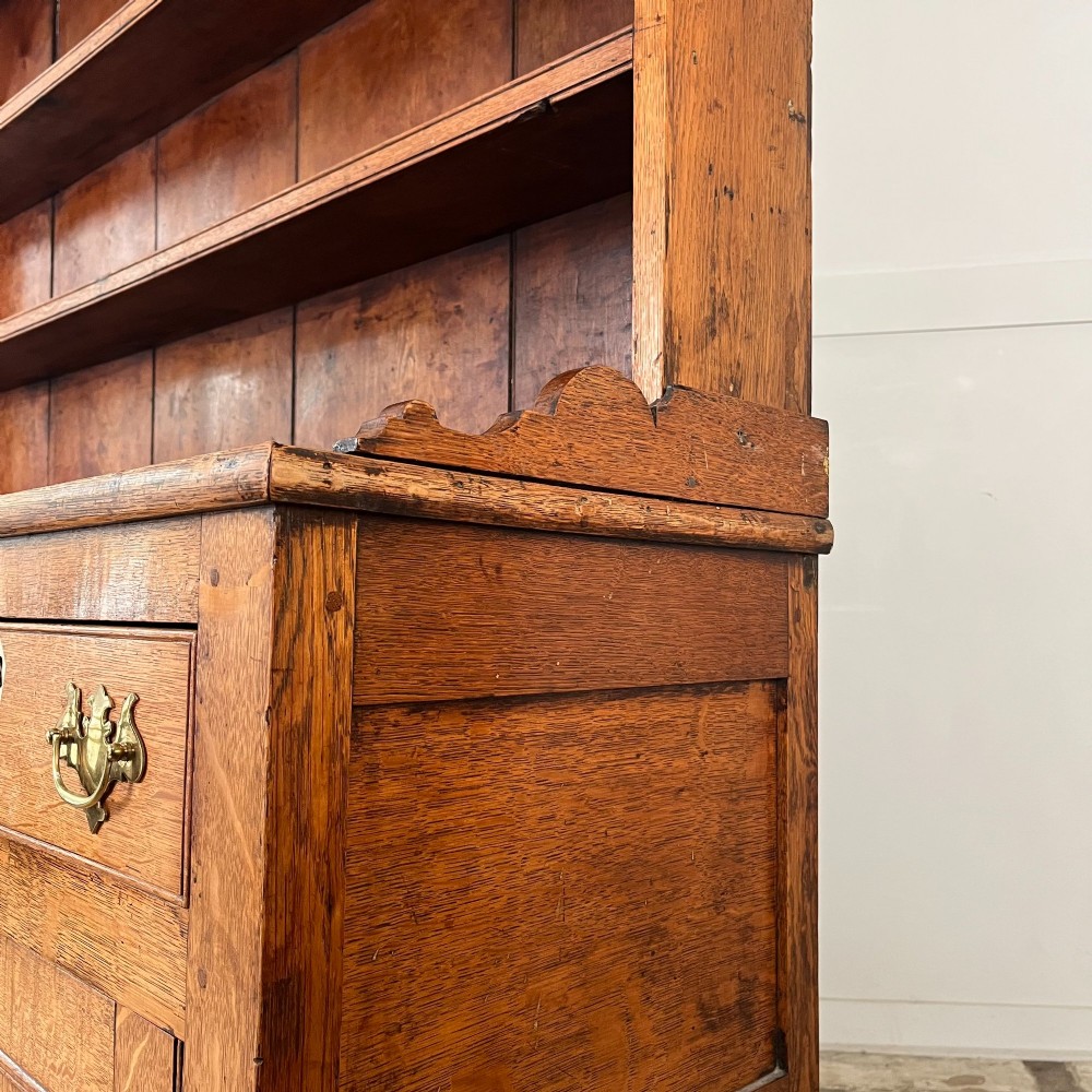 An early nineteenth-century oak kitchen dresser featuring an open upper plate rack over a base with central drawers and side cupboard doors with brass hardware. View XI