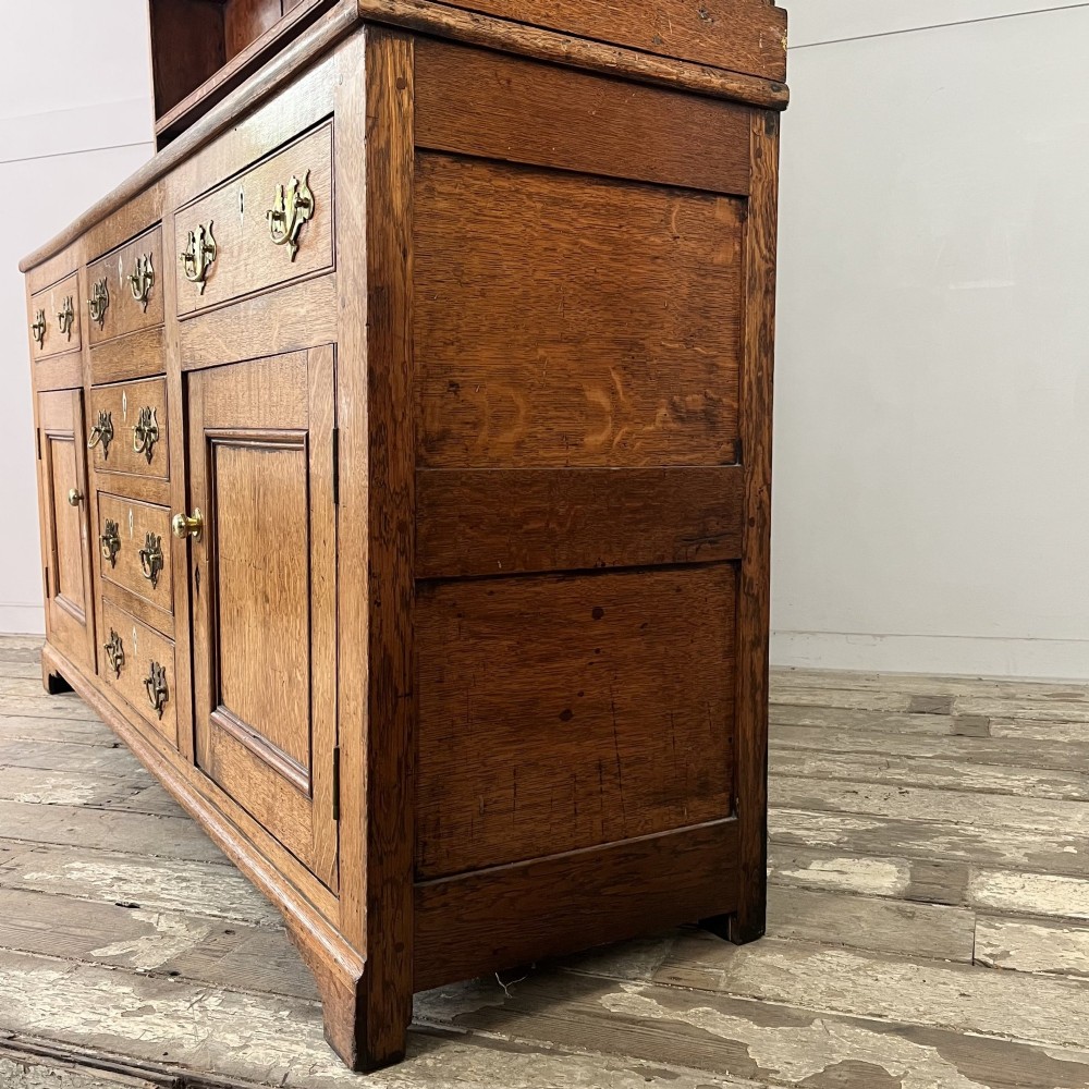 An early nineteenth-century oak kitchen dresser featuring an open upper plate rack over a base with central drawers and side cupboard doors with brass hardware. View XII