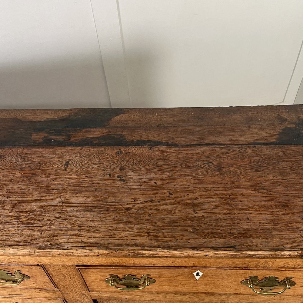 An early nineteenth-century oak kitchen dresser featuring an open upper plate rack over a base with central drawers and side cupboard doors with brass hardware. View XIII
