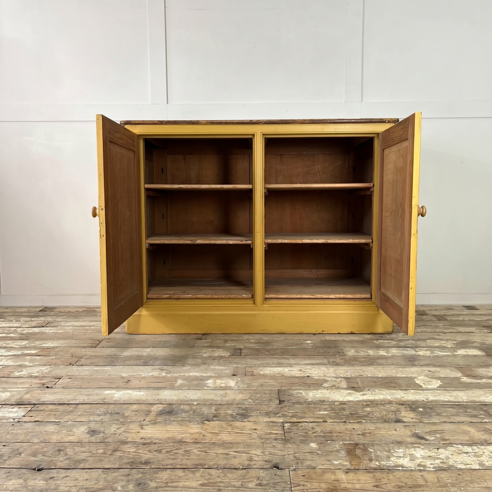 A large Victorian pine school cupboard featuring a mustard yellow painted finish, two panelled doors with wooden knobs, and a dark waxed wooden top. View II
