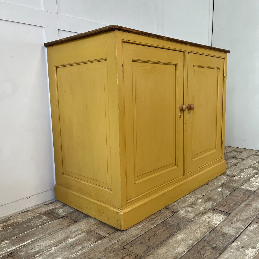 A large Victorian pine school cupboard featuring a mustard yellow painted finish, two panelled doors with wooden knobs, and a dark waxed wooden top. View III