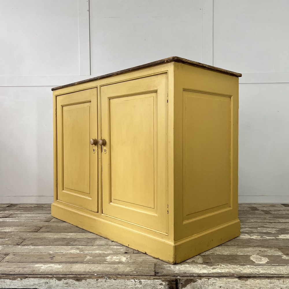 A large Victorian pine school cupboard featuring a mustard yellow painted finish, two panelled doors with wooden knobs, and a dark waxed wooden top. View IV