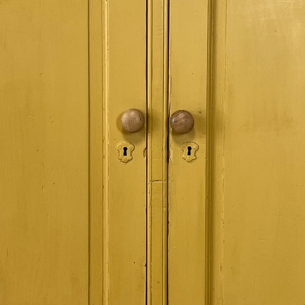 A large Victorian pine school cupboard featuring a mustard yellow painted finish, two panelled doors with wooden knobs, and a dark waxed wooden top. View V
