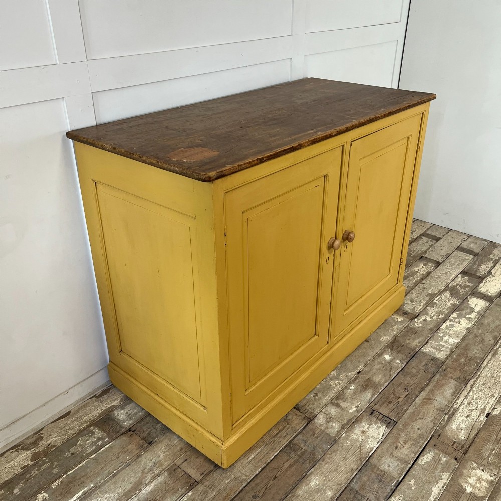 A large Victorian pine school cupboard featuring a mustard yellow painted finish, two panelled doors with wooden knobs, and a dark waxed wooden top. View VI
