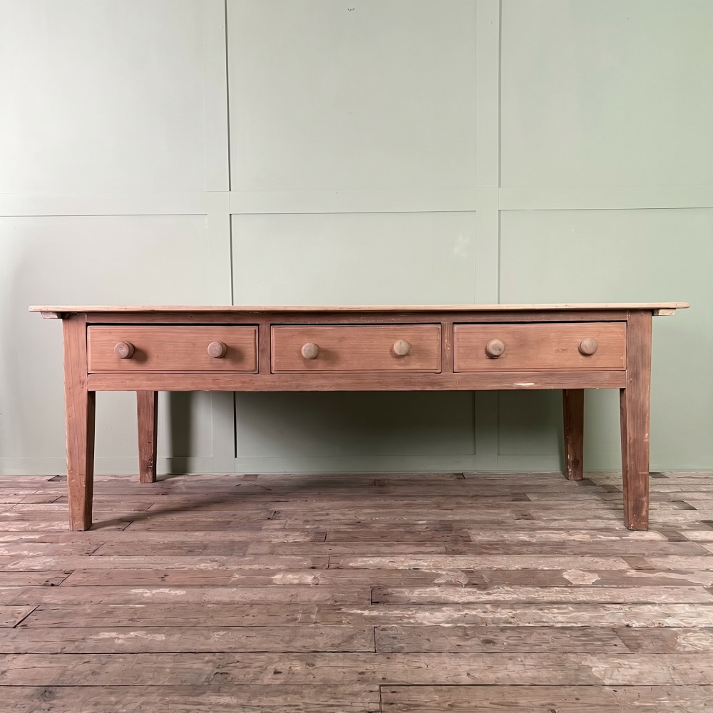 An early nineteenth-century timber prep table featuring three drawers with round wooden knobs set above four tapered legs.