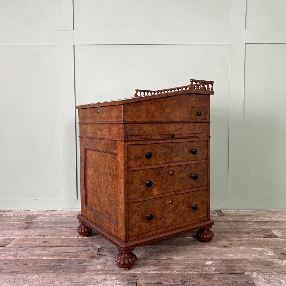 A 19th-century burr walnut Davenport desk featuring a sloped writing lid with a spindled gallery rail, side drawers, and turned feet.