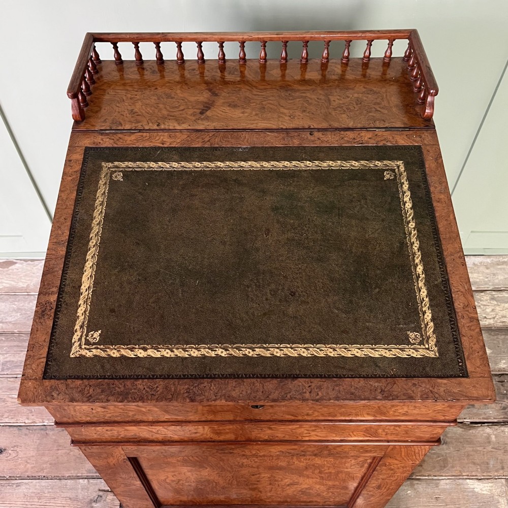 A 19th-century burr walnut Davenport desk featuring a sloped writing lid with a spindled gallery rail, side drawers, and turned feet. View IV