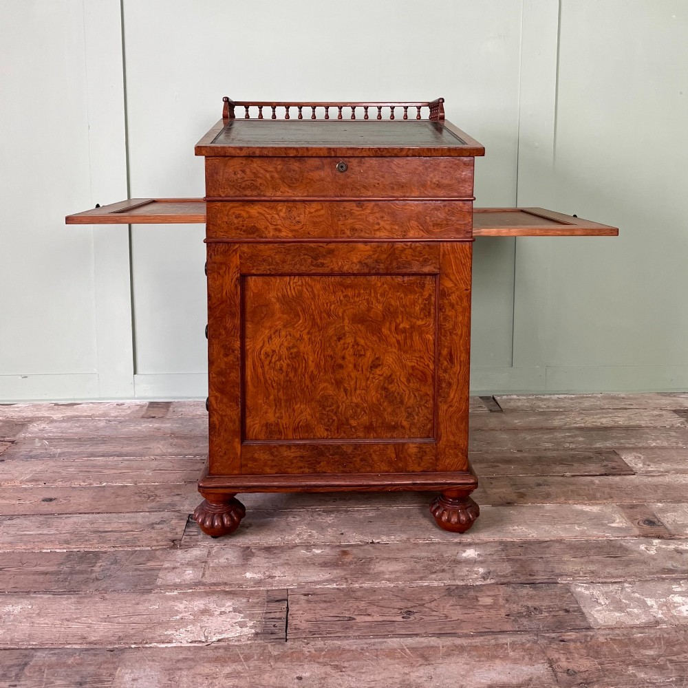 A 19th-century burr walnut Davenport desk featuring a sloped writing lid with a spindled gallery rail, side drawers, and turned feet. View V