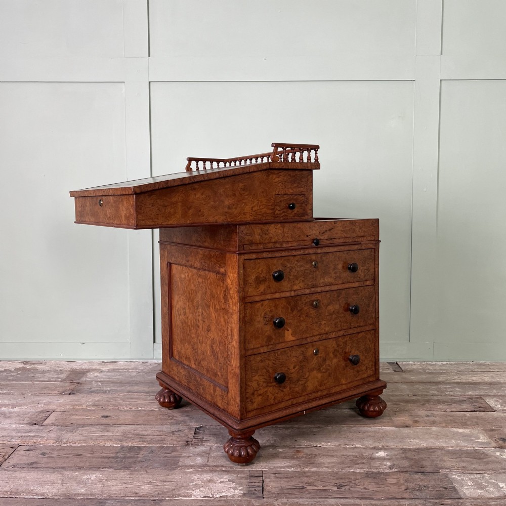 A 19th-century burr walnut Davenport desk featuring a sloped writing lid with a spindled gallery rail, side drawers, and turned feet. View VI