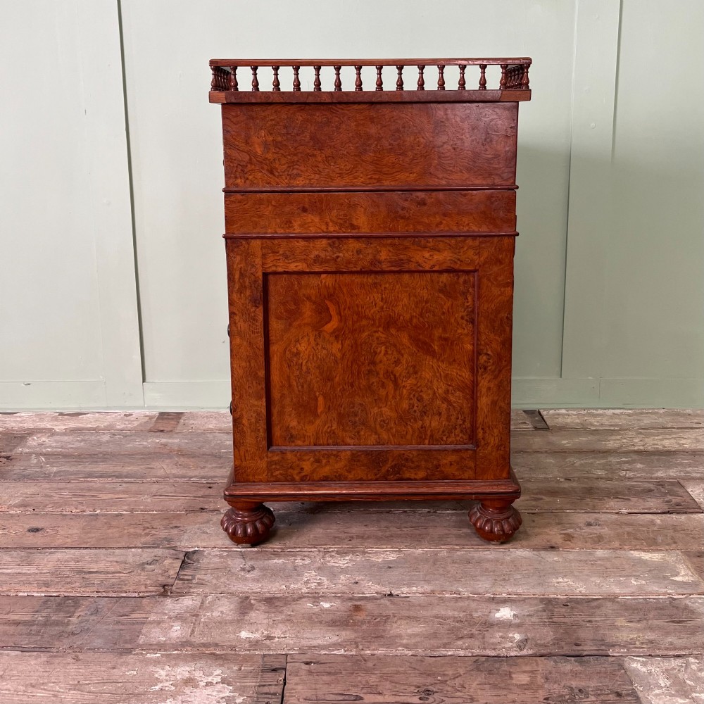 A 19th-century burr walnut Davenport desk featuring a sloped writing lid with a spindled gallery rail, side drawers, and turned feet. View X