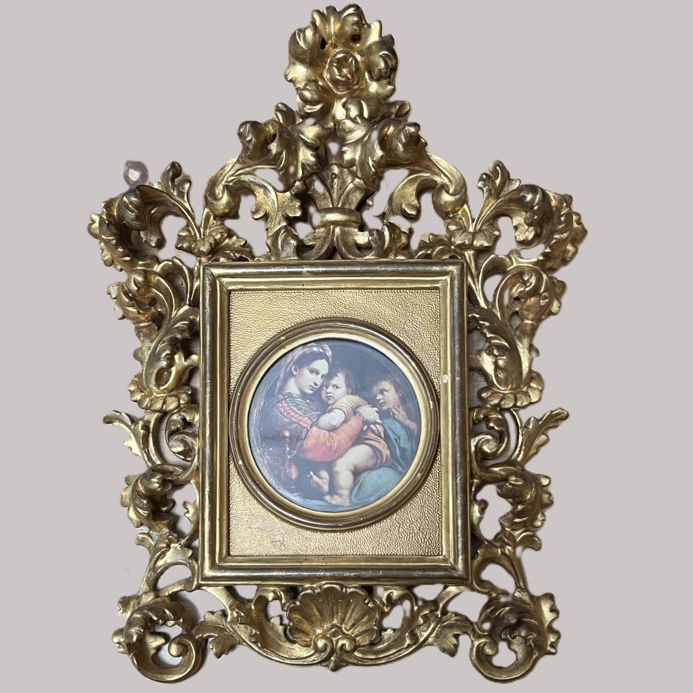 A 19th-century Florentine carved giltwood picture frame featuring openwork acanthus leaves, scrollwork cresting, and a central circular image of the Madonna and Child.