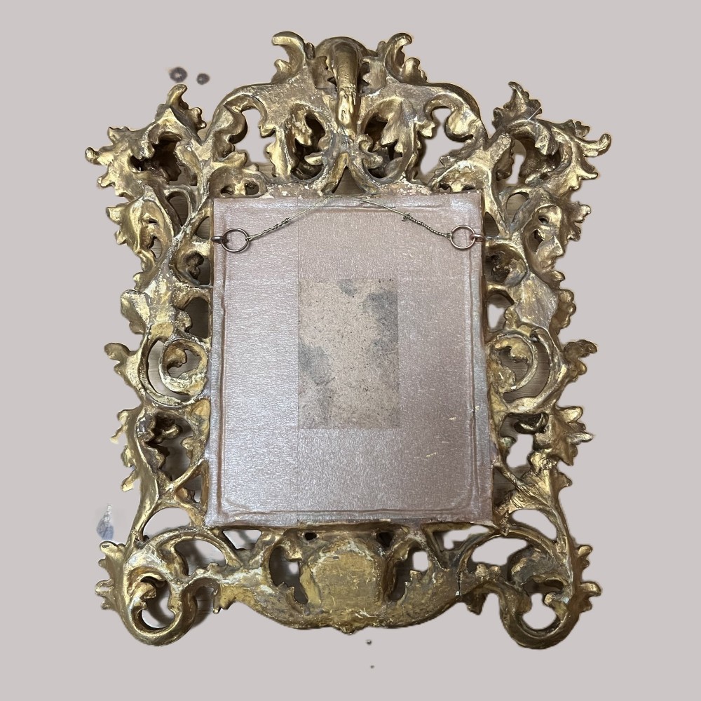 A 19th-century Florentine carved giltwood picture frame featuring openwork acanthus leaves, scrollwork cresting, and a central circular image of the Madonna and Child. View III