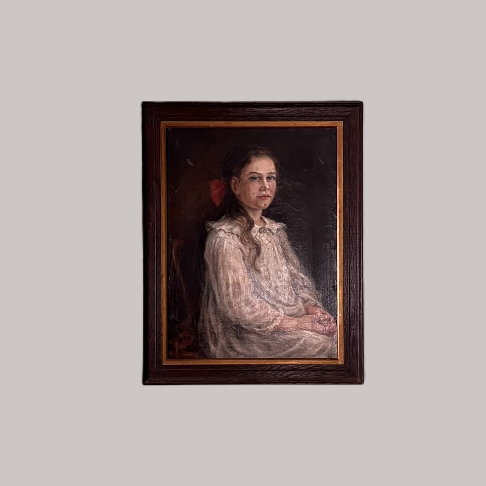 An Edwardian oil painting on canvas featuring a seated young girl in a cream lace-collared dress, housed in a dark wooden frame with a gold inner slip.