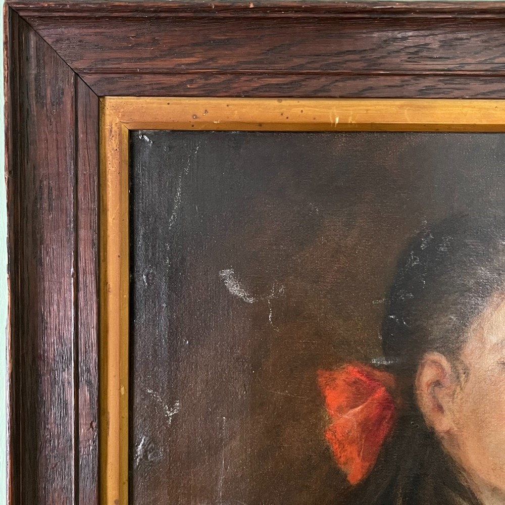 An Edwardian oil painting on canvas featuring a seated young girl in a cream lace-collared dress, housed in a dark wooden frame with a gold inner slip. View V