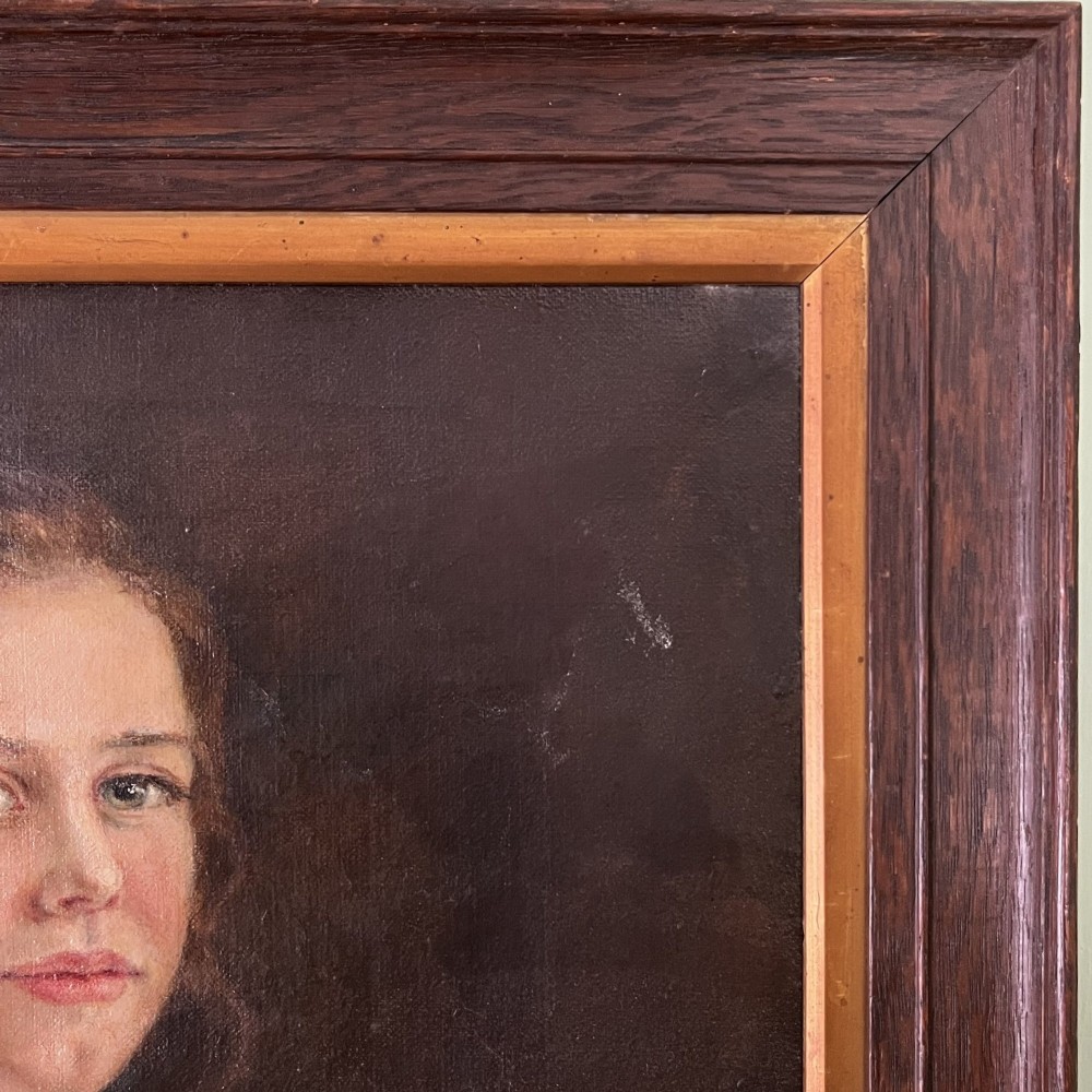 An Edwardian oil painting on canvas featuring a seated young girl in a cream lace-collared dress, housed in a dark wooden frame with a gold inner slip. View VI