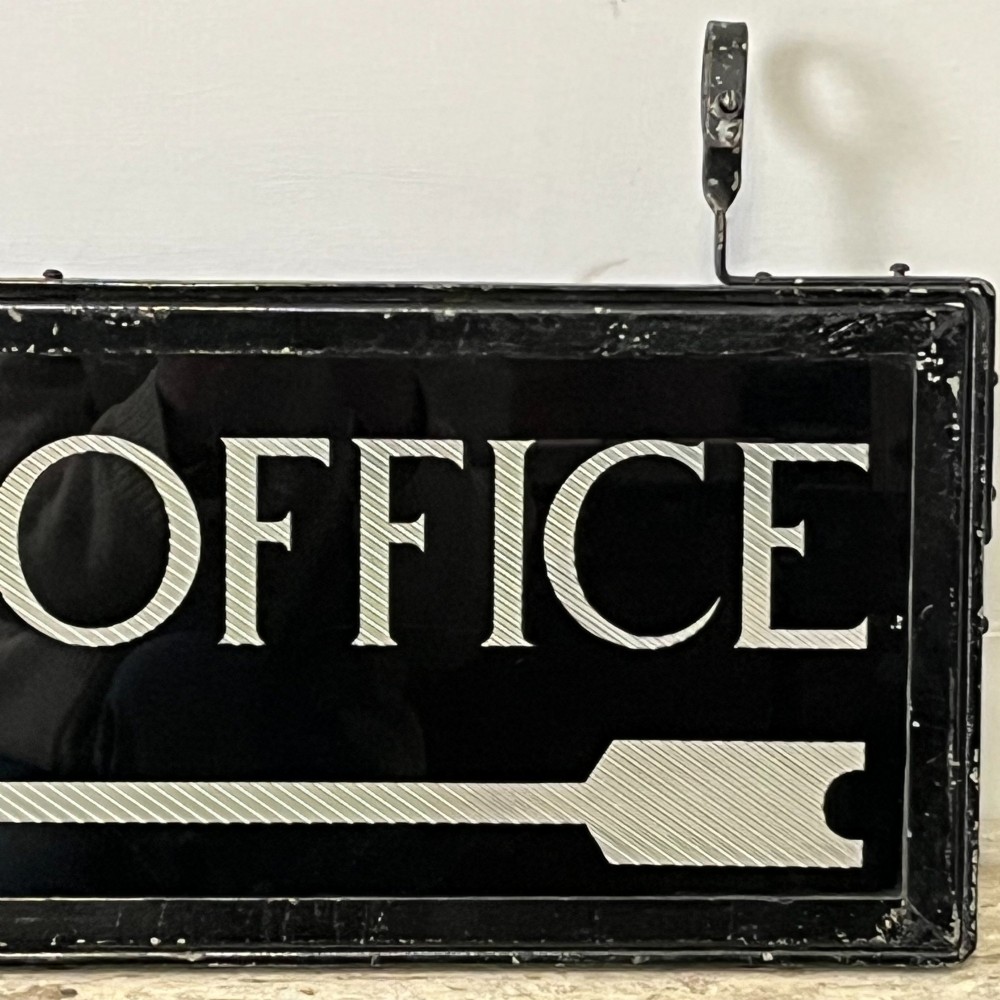 A rectangular double-sided black glass directional sign featuring white lettering that reads POST OFFICE above a striped directional arrow, mounted in a dark iron frame with top loops. View II